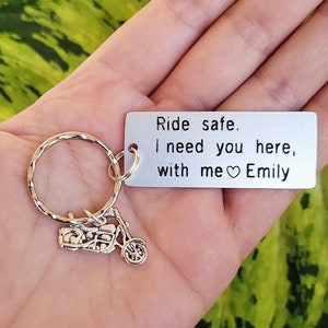 May include: Silver motorcycle keychain with a rectangular tag. The tag reads "Ride safe. I need you here, with me Emily" in black text. The keychain has a silver ring and a small motorcycle charm.