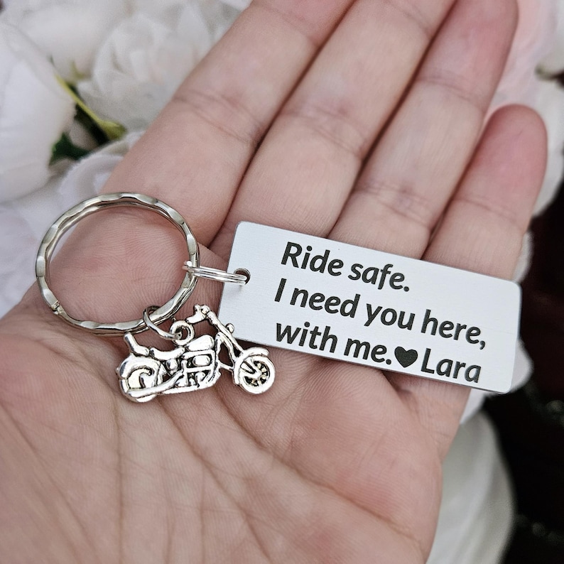 May include: Silver motorcycle keychain with a rectangular tag. The tag reads "Ride safe. I need you here, with me. Lara." The keychain has a textured ring and a small motorcycle charm.