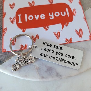 May include: A silver motorcycle keychain with a rectangular tag that reads "Ride safe. I need you here, with me Monique" next to a card that says "I love you!" in a speech bubble.