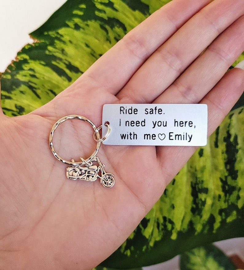 May include: Silver motorcycle keychain with a rectangular tag. The tag reads "Ride safe. I need you here, with me Emily" in black text. The keychain has a silver ring and a small motorcycle charm.