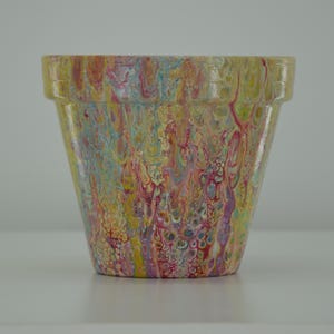 Könnte beinhalten: Ein gelber Terrakotta-Blumentopf mit einem farbenfrohen abstrakten Design in Rosa-, Blau- und Gelbtönen.