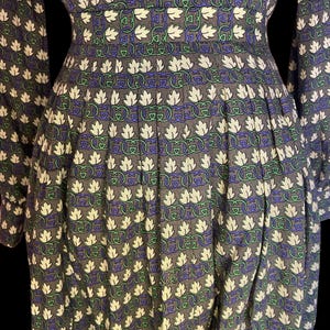 May include: A gray dress with a repeating pattern of white leaves, green and blue interlocking designs. The dress has long sleeves and a fitted waist, with pleats in the skirt. The fabric appears to be a soft material.