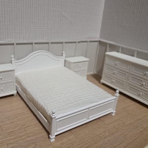 May include: A miniature white bedroom furniture set consisting of a bed with a textured white cover, two matching bedside tables with two drawers each, and a long dresser with six drawers, all featuring decorative molding and small round knobs.