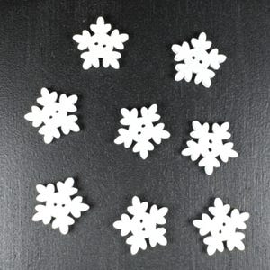 May include: Eight white snowflake buttons with a six-pointed star design. The buttons are arranged in a scattered pattern on a black background.