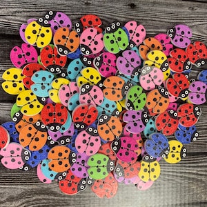 May include: A collection of colorful wooden ladybug buttons in various shades of red, yellow, blue, green, and pink. The buttons are all shaped like ladybugs with black spots and have a flat back.