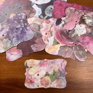 Puede incluir: Un conjunto de 10 etiquetas de papel con estampado floral de estilo vintage con bordes festoneados y dos agujeros para cuerda o cinta. Las etiquetas son en tonos de rosa, morado y verde.