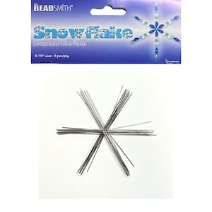 Puede incluir: Un paquete de Beadsmith Snowflake Ornament Wire Form. El paquete azul y blanco lleva las palabras "Snowflake" y "Ornament Wire Form". Contiene una forma de copo de nieve de alambre plateado, de 9,5 cm de ancho.