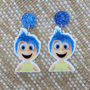 May include: A pair of drop earrings featuring the character Joy from the animated film Inside Out. Each earring has a blue glitter circle stud and a cutout of Joy with blue hair, a yellow top, and a smiling face.