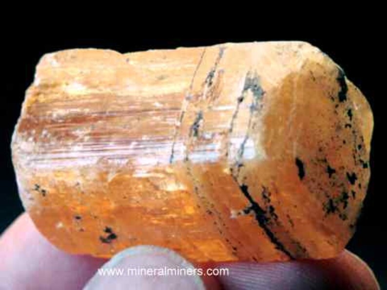 May include: A large, orange-brown, translucent crystal with striations and black inclusions. The crystal is a natural mineral specimen.