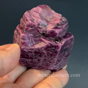 May include: A large, rough, pink ruby crystal with a deep red hue. The crystal has a natural, unpolished appearance and is a beautiful example of this gemstone.