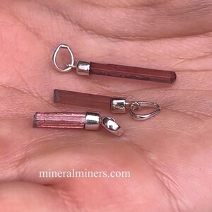 May include: Three pink tourmaline crystal pendants with silver bail settings. The pendants are different sizes and shades of pink.