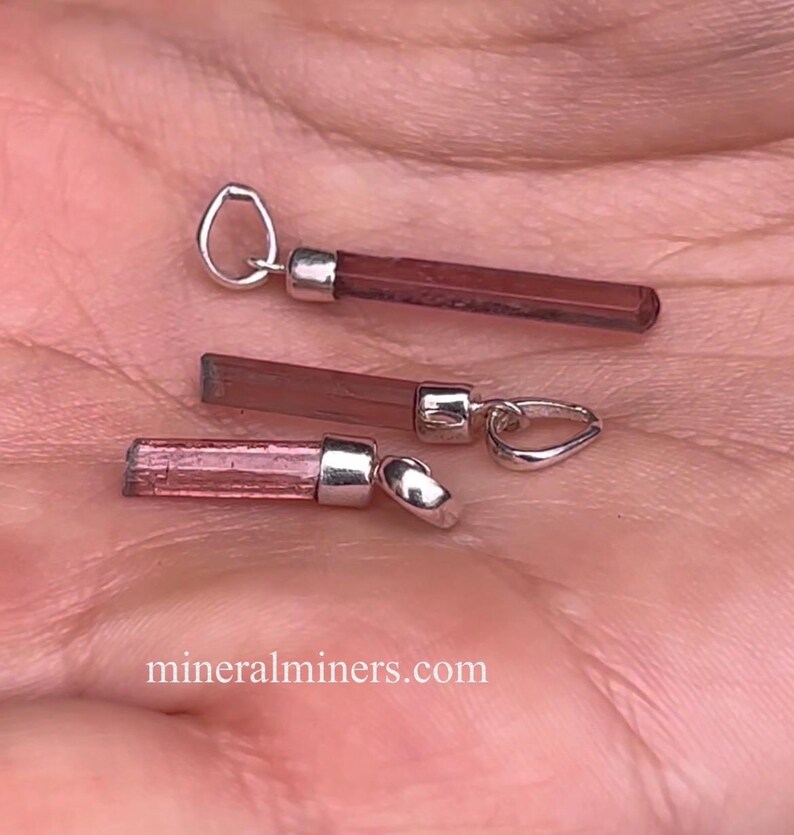 May include: Three pink tourmaline crystal pendants with silver bail settings. The pendants are different sizes and shades of pink.
