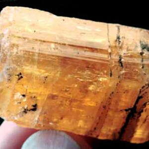 May include: A large, translucent, orange-brown crystal with black inclusions. The crystal is faceted and has a rectangular shape.