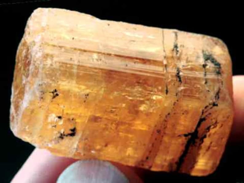 May include: A large, translucent, orange-brown crystal with black inclusions. The crystal is faceted and has a rectangular shape.