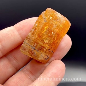 May include: A large, orange, translucent crystal with striations and inclusions. The crystal is a natural specimen and has a rough, unpolished surface.