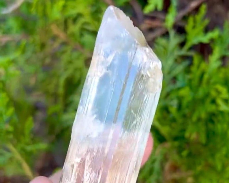 May include: A clear, translucent crystal point with a slightly yellow hue. The crystal has a smooth, polished surface and is approximately 3 inches long.