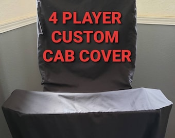 May include: Black custom cab cover with the text "4 PLAYER CUSTOM CAB COVER" in red. The cover is designed to fit over a game cabinet, with a draped design. The cover is made of a dark, possibly waterproof material.