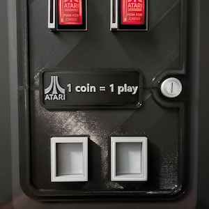 May include: Black arcade machine panel with the Atari logo and the text "1 coin = 1 play." Two red illuminated buttons read "PUSH FOR CREDIT." Below are two square coin return slots. The Atari logo is at the bottom.
