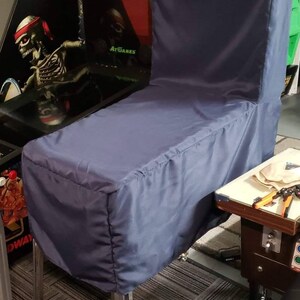 May include: A navy blue pinball machine cover. The cover is made of a smooth fabric and is designed to fit over the entire machine, including the backbox. The cover is supported by chrome legs.
