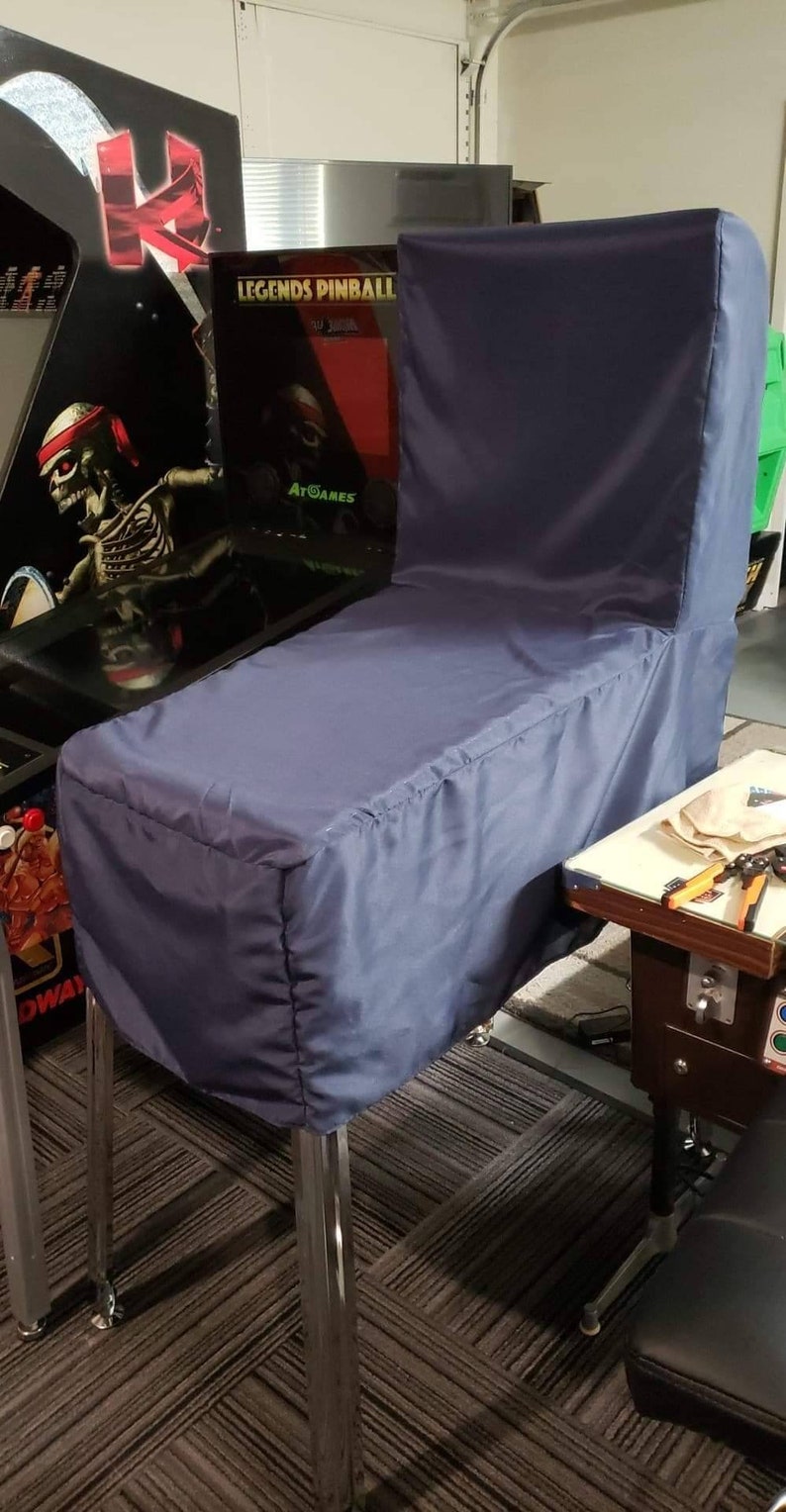 May include: A navy blue pinball machine cover. The cover is made of a smooth fabric and is designed to fit over the entire machine, including the backbox. The cover is supported by chrome legs.