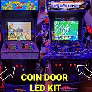 May include: Two arcade game machines side-by-side. The left machine displays "Marvel vs. Capcom 2" and the right machine displays "NFL Blitz". Both machines have coin door LED kits installed, with the text "COIN DOOR LED KIT" at the bottom.