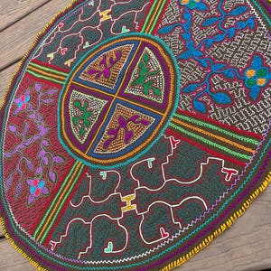 May include: A circular textile piece featuring intricate embroidery in vibrant colors including blue, purple, green, and orange. The design is divided into quadrants with a central circular motif, all bordered by a bright yellow stitched edge.