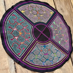 May include: A circular black fabric wall hanging with a geometric design embroidered in various colors, including pink, purple, blue, green, and yellow.