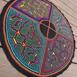 May include: A circular black fabric piece featuring intricate, multi-colored embroidery in four distinct quadrants. The design includes complex geometric patterns in shades of neon green, pink, blue, and orange, separated by a central black circle.