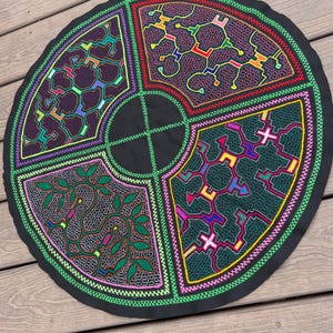 May include: A circular black fabric piece featuring intricate, colorful embroidery divided into four distinct quadrants. Each section displays unique geometric and organic patterns in vibrant neon threads, including green, pink, yellow, and blue.