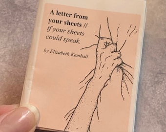 May include: A small, folded booklet with a light pink cover. The cover features black text that reads "A letter from your sheets // if your sheets could speak. by Elizabeth Kemball." A black and white illustration of a hand grasping fabric is also present.