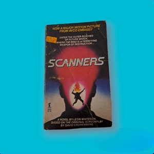 Puede incluir: Una portada de libro de bolsillo para la novela "Scanners" de Leon Whiteson. La portada presenta un fondo rojo y naranja con una silueta de una persona con una llama sobre su cabeza. El texto "Scanners" está en letras blancas grandes en la parte superior de la portada. El texto "Now a major motion picture from Avco Embassy" está en la parte superior de la portada. El texto "A novel by Leon Whiteson, based on the original screenplay by David Cronenberg" está en la parte inferior de la portada.