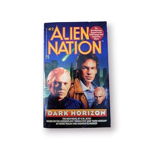 Può includere: Una copertina di un libro tascabile per il romanzo "Alien Nation: Dark Horizon" di K.W. Jeter. La copertina presenta una città con tre uomini, uno con la pelle rossa, uno con una camicia blu e uno con una camicia nera. Il libro è basato sulle sceneggiature "Green Eyes" e "Dark Horizon" di Diane Frolov e Andrew Schneider.
