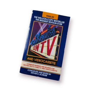 Puede incluir: Un libro antiguo titulado "Movies on TV and Videocassette" de 1988-89. La portada es azul con un diseño de neón en rojo y blanco. El libro incluye calificaciones y reseñas completas de películas en TV, cable y videocasetes.