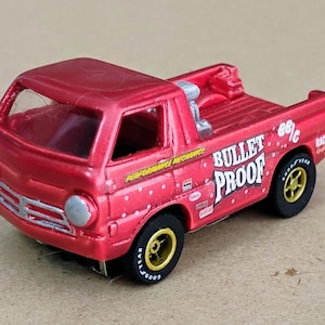 May include: A red toy pickup truck with the words "BULLET PROOF" in white lettering on the side. The truck has black tires with gold rims and the text "GOODYEAR". The truck has the text "PERFORMANCE MECHANICS" on the side.