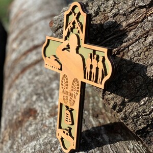 Może przedstawiać: Drewniany krzyż z zielonym tłem. Krzyż przedstawia sylwetkę żołnierza salutującego, czołg, buty z napisem "ARMY" i identyfikator.