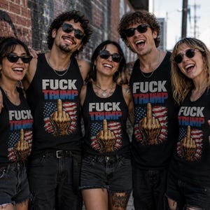 K&ouml;nnte beinhalten: F&uuml;nf Personen tragen schwarze Tanktops mit dem Text "FUCK TRUMP" in Rot und Blau, sowie ein Bild einer Hand, die den Mittelfinger &uuml;ber einer amerikanischen Flagge zeigt. Sie l&auml;cheln und tragen Sonnenbrillen.