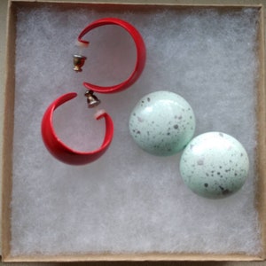 May include: A set of earrings featuring two red hoop earrings and two round, speckled green earrings.