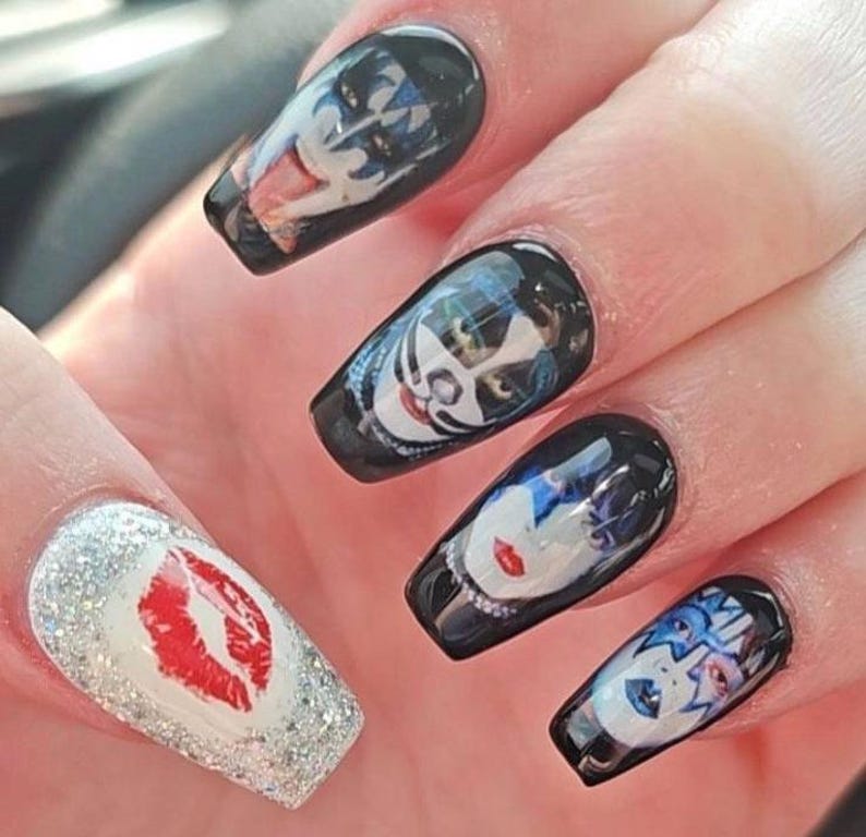May include: Black acrylic nails with images of the band KISS. One nail features a red lip print on a silver glitter background. The other nails have images of the band members' faces.