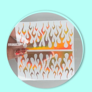 May include: Two sheets of white nail art stencils with a repeating pattern of flame shapes. The stencils are on a holographic background with orange, yellow, and pink colors.