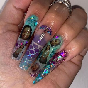 Peut inclure: Longues ongles en acrylique transparent avec un th&egrave;me sir&egrave;ne. Chaque ongle est d&eacute;cor&eacute; d'un motif diff&eacute;rent, y compris des paillettes, des coquillages et de petites images d'enfants.