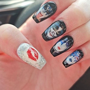 Peut inclure: Gros plan sur une main avec cinq ongles longs, noirs et blancs. Les ongles sont d&eacute;cor&eacute;s d'images du groupe KISS. Un ongle a une finition argent&eacute;e paillet&eacute;e avec une empreinte de l&egrave;vres rouges.