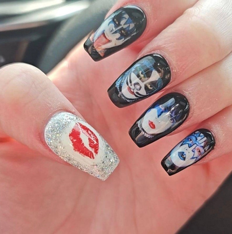 Peut inclure: Gros plan sur une main avec cinq ongles longs, noirs et blancs. Les ongles sont d&eacute;cor&eacute;s d'images du groupe KISS. Un ongle a une finition argent&eacute;e paillet&eacute;e avec une empreinte de l&egrave;vres rouges.