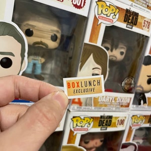 Op de afbeelding: Een verzameling Pop! Television vinyl figuren in hun originele dozen. De dozen bevatten personages uit "Stranger Things" en "The Walking Dead". Een kleine "BoxLunch Exclusive" sticker wordt voor de figuren gehouden.