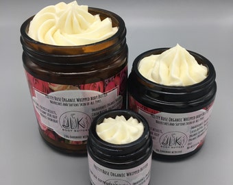 May include: Three glass jars of whipped body butter with a pink rose design and the text "Pretty Rose Organic Whipped Body Butter" on the label. The jars are different sizes and are filled with a white whipped cream.