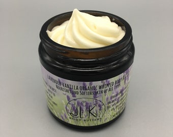 May include: A glass jar of lavender vanilla organic whipped body butter. The jar has a black label with white text that reads "Lavender Vanilla Organic Whipped Body Butter Nourishes and Softens Skin of All Types" and a logo that says "Body Butters".
