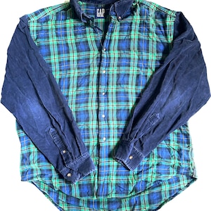 Puede incluir: Una camisa a cuadros con botones con un patrón verde y azul en el cuerpo y mangas de pana azul marino liso. La camisa tiene cuello abotonado y la marca "GAP" es visible en el cuello.