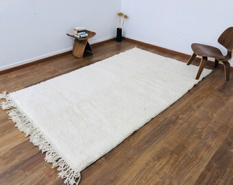 May include: A white shag rug with fringe on all sides. The rug is laid out on a hardwood floor.