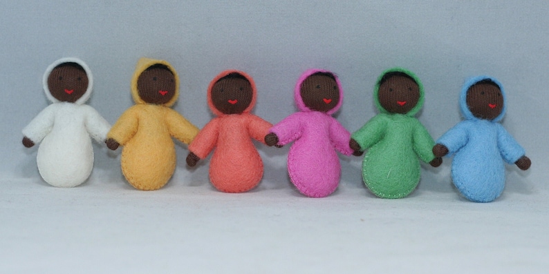Puede incluir: Siete mu&ntilde;ecas de fieltro que llevan atuendos con capucha de varios colores, entre ellos blanco, amarillo, naranja, rosa, verde y azul. Las mu&ntilde;ecas tienen caras marrones y labios rojos.