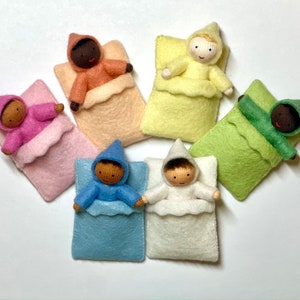 Puede incluir: Seis mu&ntilde;ecas de fieltro en sacos de dormir de diferentes colores. Las mu&ntilde;ecas tienen diferentes tonos de piel y llevan pijamas con capucha.