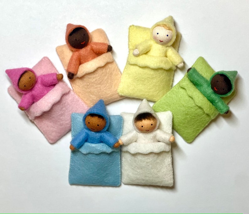 Puede incluir: Seis mu&ntilde;ecas de fieltro en sacos de dormir de diferentes colores. Las mu&ntilde;ecas tienen diferentes tonos de piel y llevan pijamas con capucha.